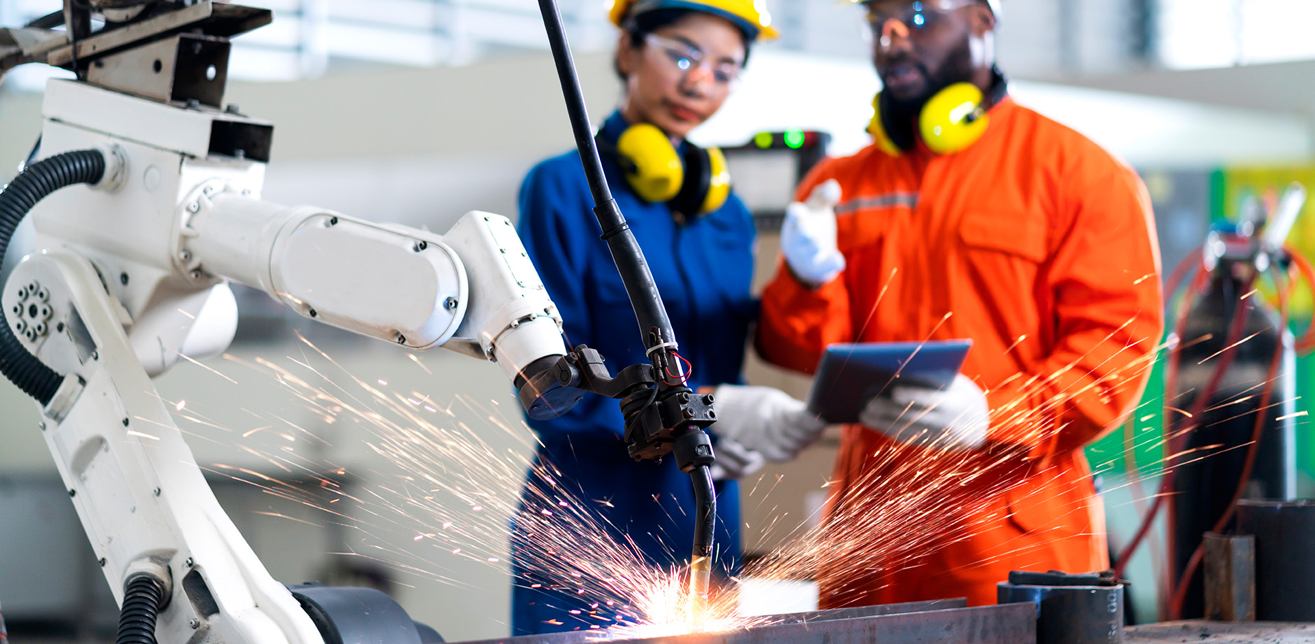Workers address concerns looking at a tablet while a robot does welding work